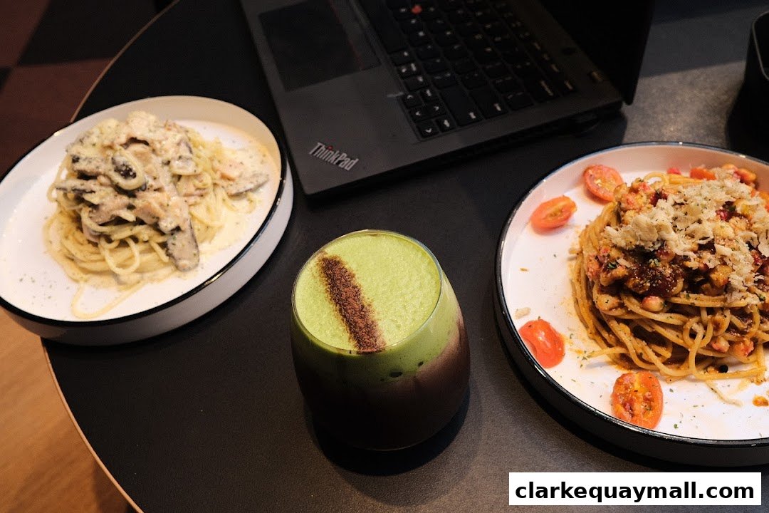 Two plates of pasta and a green drink sit on a table next to a laptop.