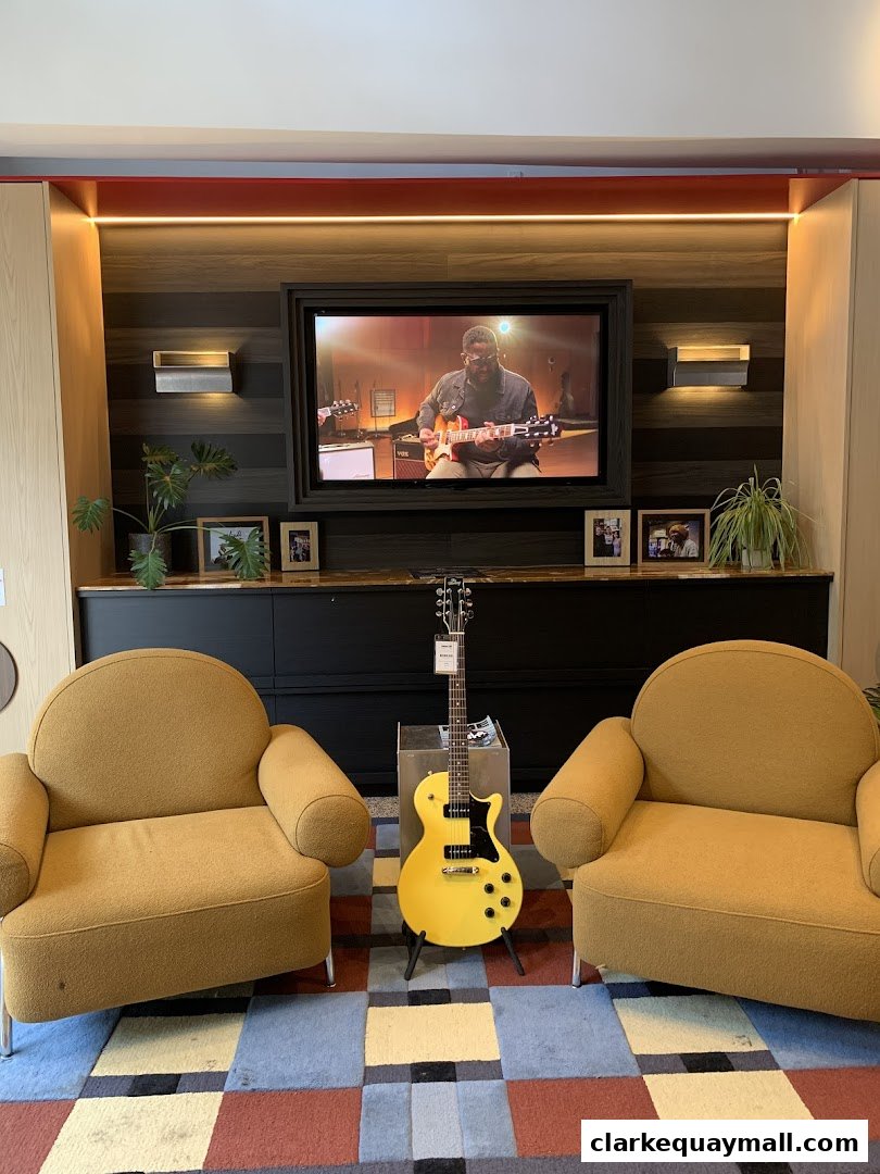 A yellow electric guitar is displayed between two yellow chairs in front of a screen showing a musician playing guitar.