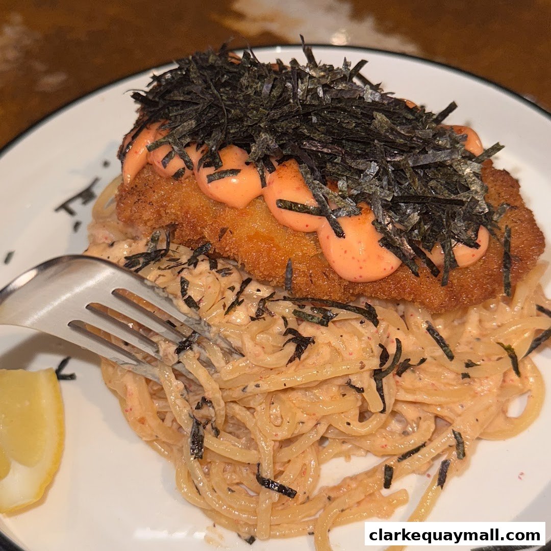A close-up of a creamy pasta dish topped with fried fish, seaweed, and sauce.