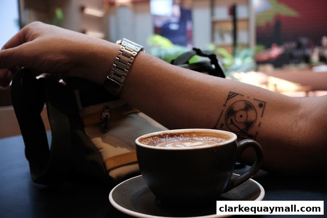 A person's arm with a watch and tattoo rests near a cup of coffee.