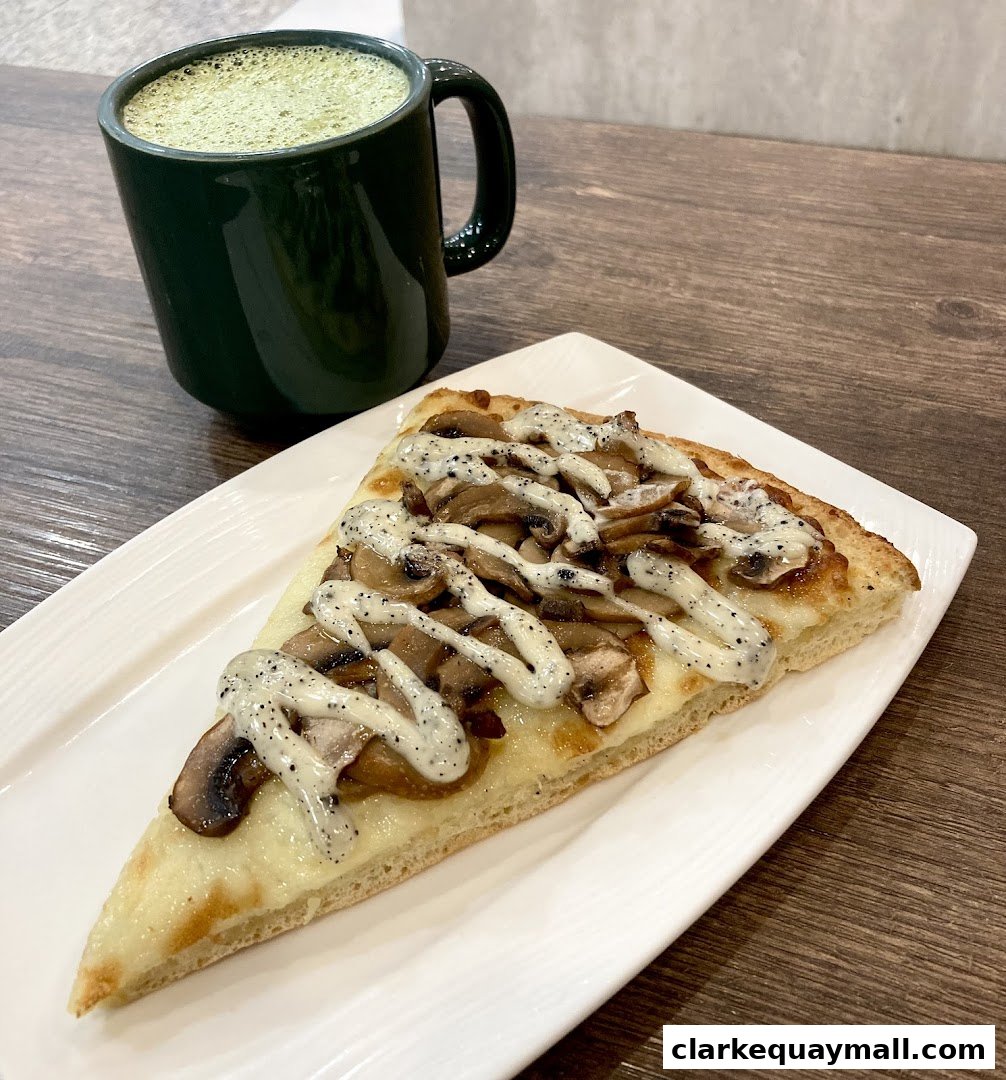 A slice of mushroom pizza with a drizzle of sauce and a mug of green tea.