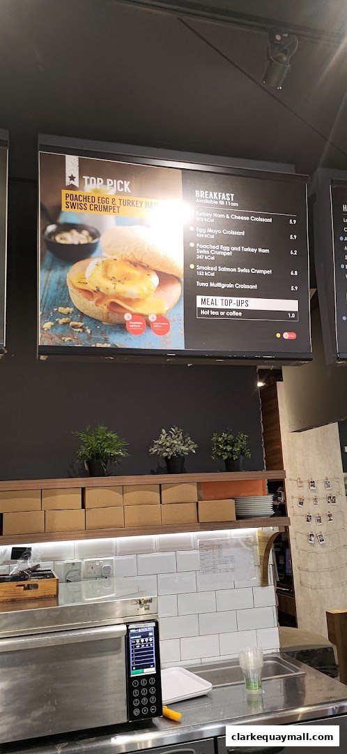 A digital menu board displaying breakfast items and meal top-ups at Swissbake Cafe.