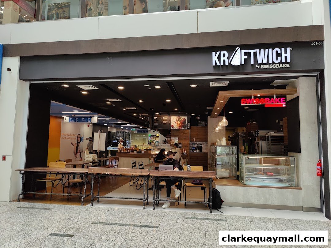 The exterior of Swissbake Cafe, featuring a modern design with seating and a prominent "KRAFTWICH by SWISSBAKE" sign.
