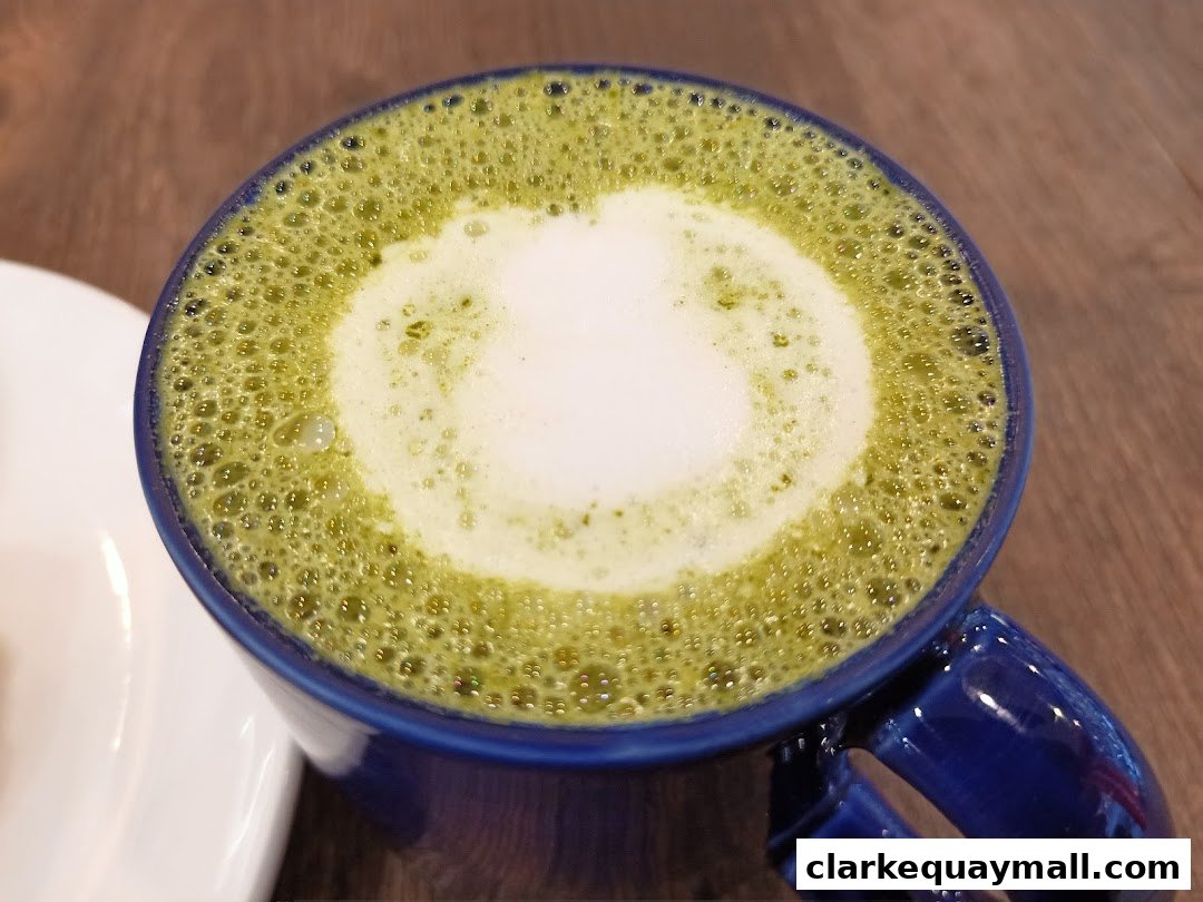 A close-up shot of a frothy matcha latte in a blue mug on a wooden surface.