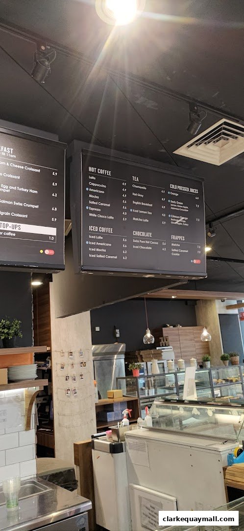 A menu board displaying hot coffee, iced coffee, tea, chocolate, frappes, and cold-pressed juices with prices.