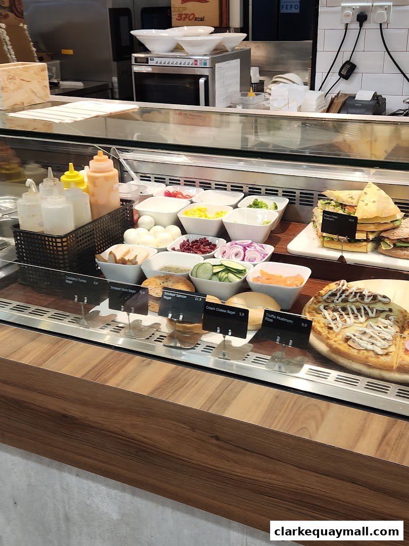 A display case filled with fresh ingredients, bagels, sandwiches, and a pizza.