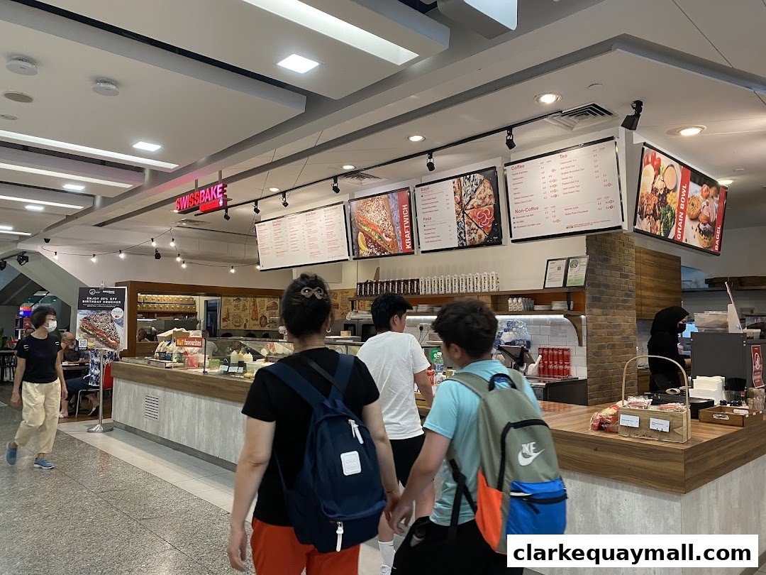 People walking past a Swissbake Cafe counter with menus and food displays.