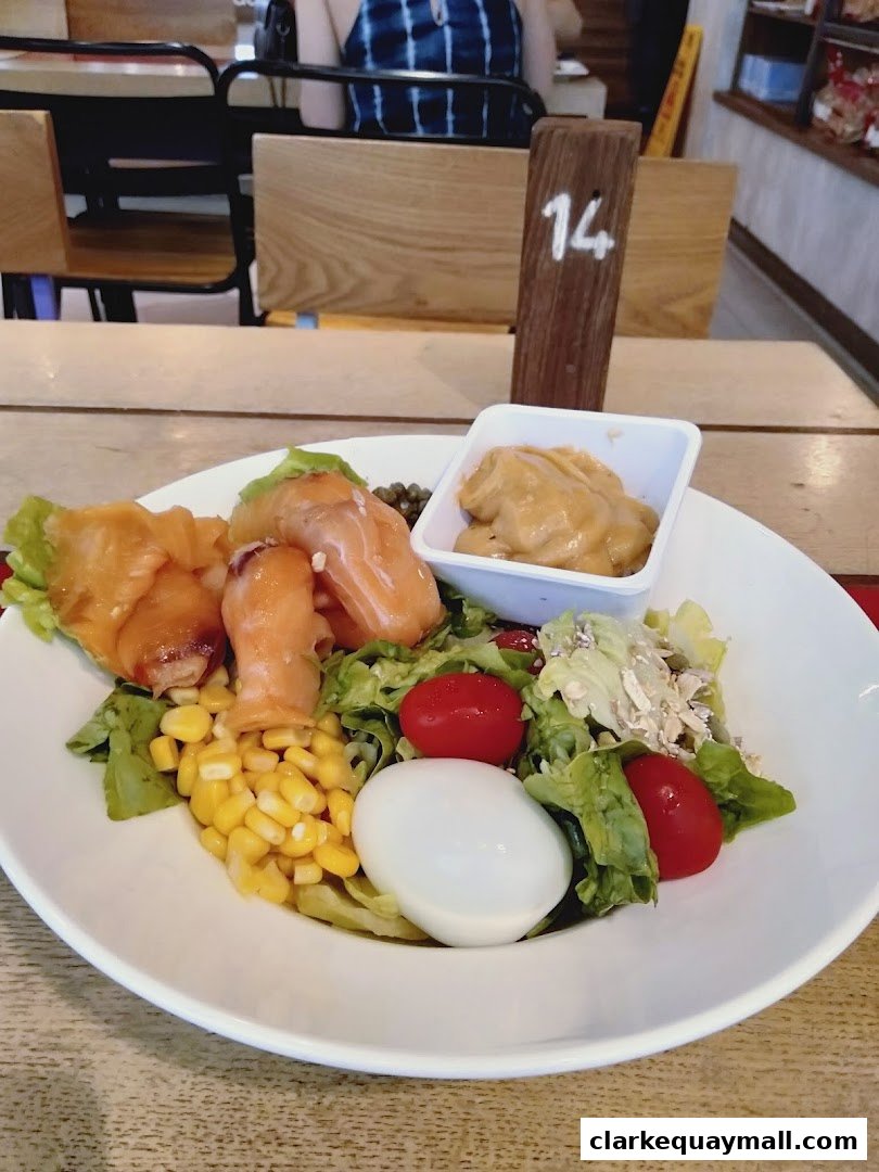 A delicious salmon salad with corn, egg, tomatoes, and a side of dressing.