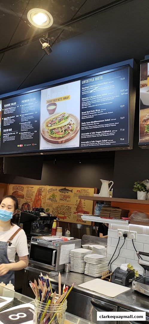 A digital menu board displaying various salads and wraps with prices and descriptions.