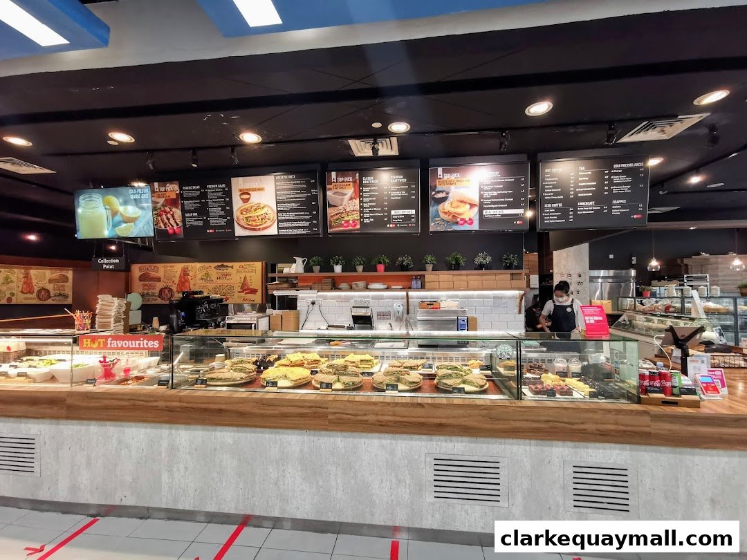 A view of the Swissbake Cafe counter displaying sandwiches, cakes, and drinks with menu boards above.