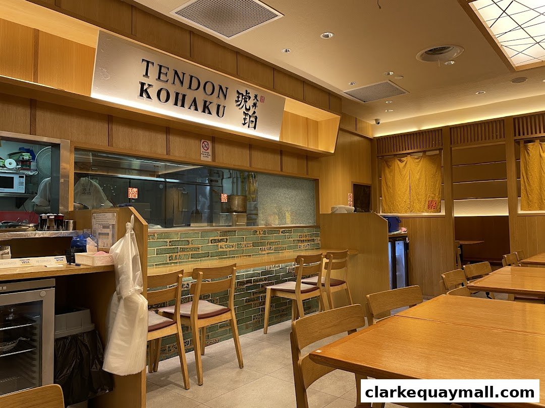 Interior view of Tendon Kohaku restaurant with wooden tables, chairs, and a view into the kitchen.