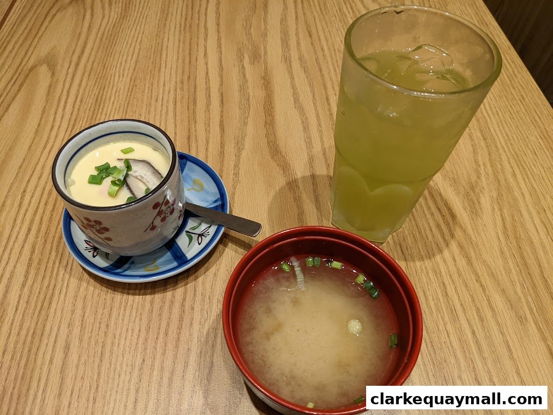 A Japanese meal featuring chawanmushi, miso soup, and a green beverage on a wooden table.