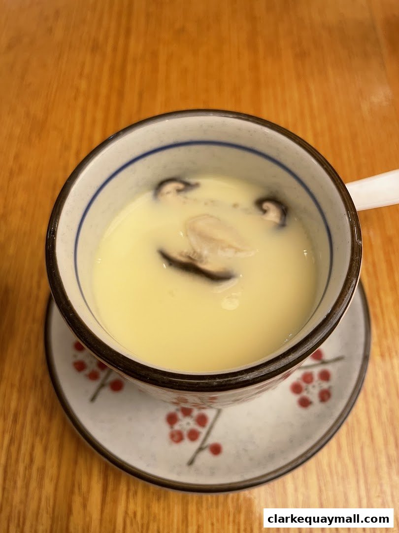 A close-up of a steaming bowl of chawanmushi with mushrooms and a piece of seafood.