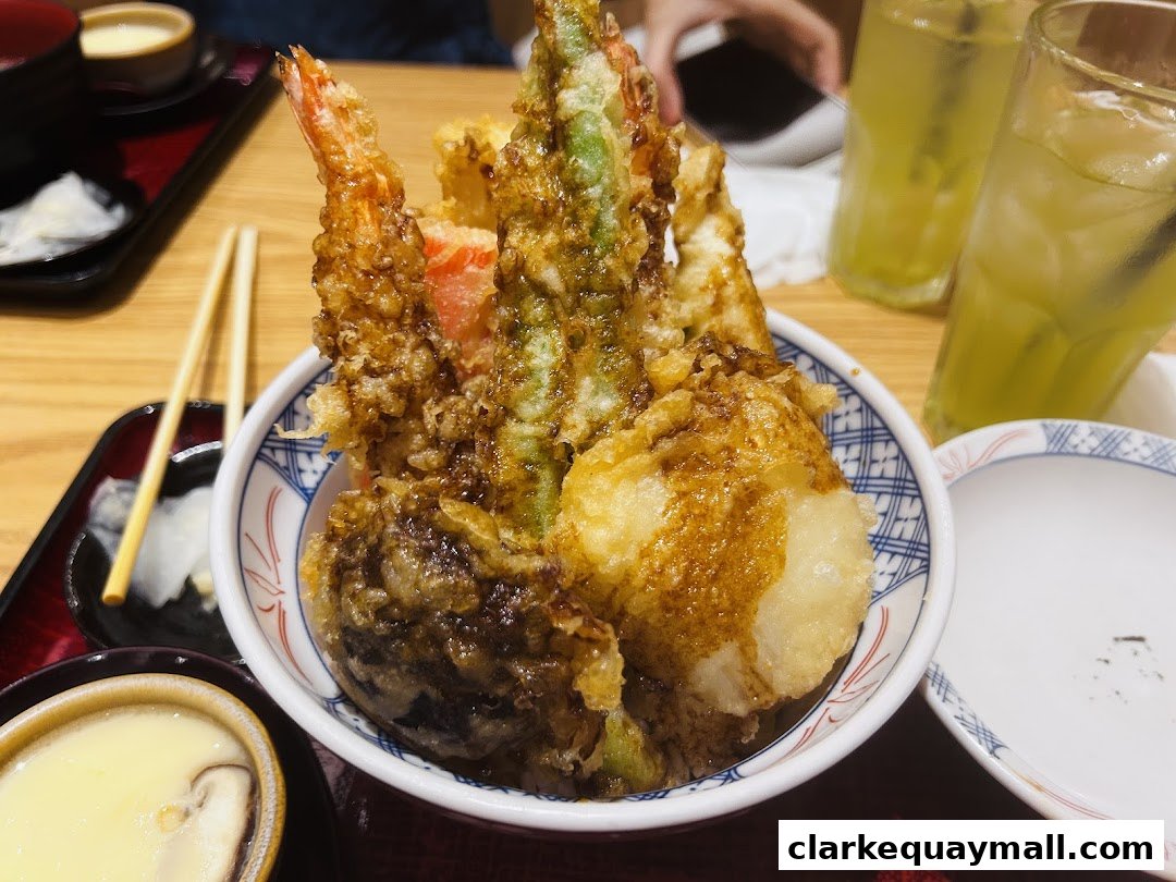 A close-up of a delicious tempura bowl with shrimp, vegetables, and rice, served with drinks.