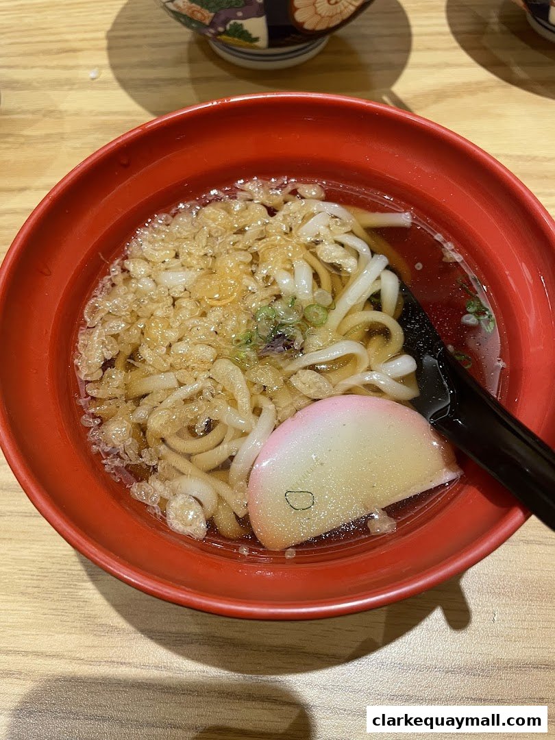 A close-up shot of a steaming bowl of udon noodles with tempura flakes and fish cake.