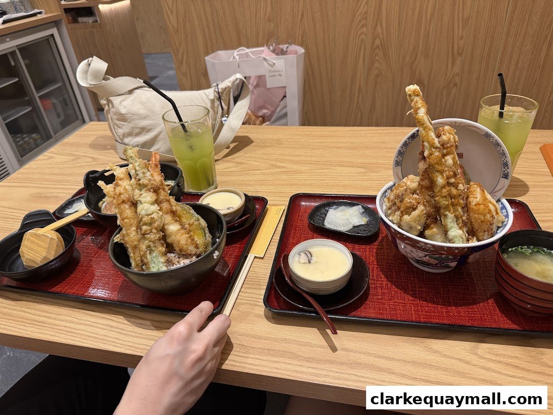 Two bowls of tempura donburi with sides and drinks on a wooden table.