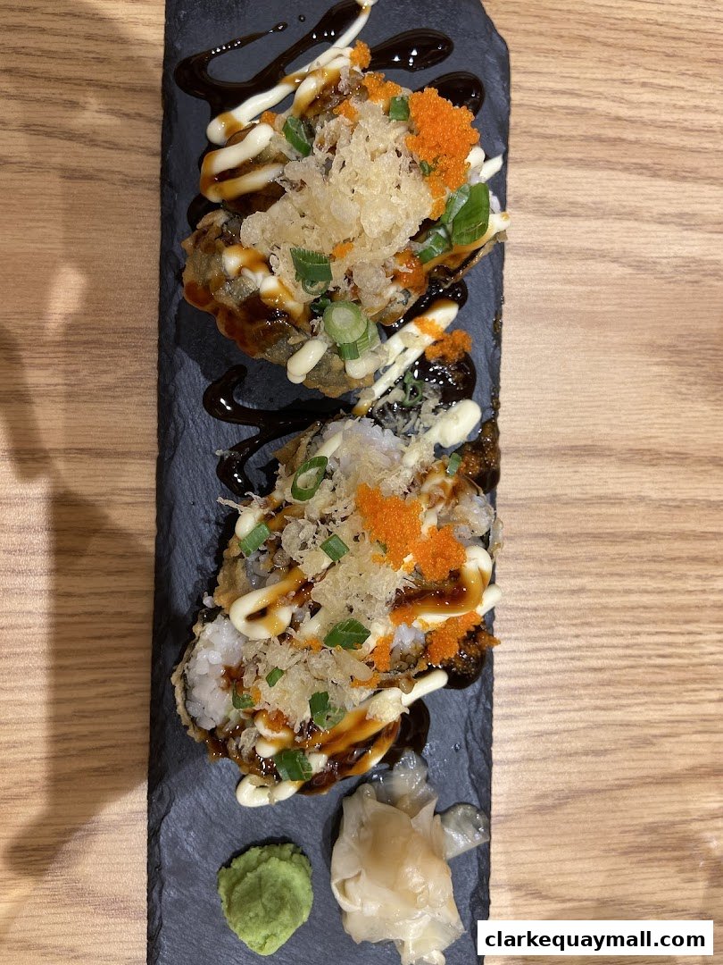 Two pieces of crispy fried sushi rolls topped with sauce, scallions, and roe, served with wasabi and ginger.
