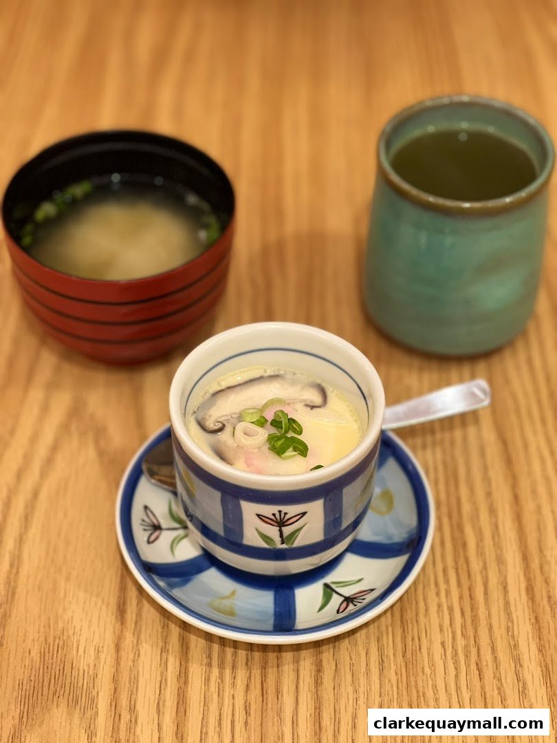 A close-up of a Japanese steamed egg custard dish with soup and green tea.