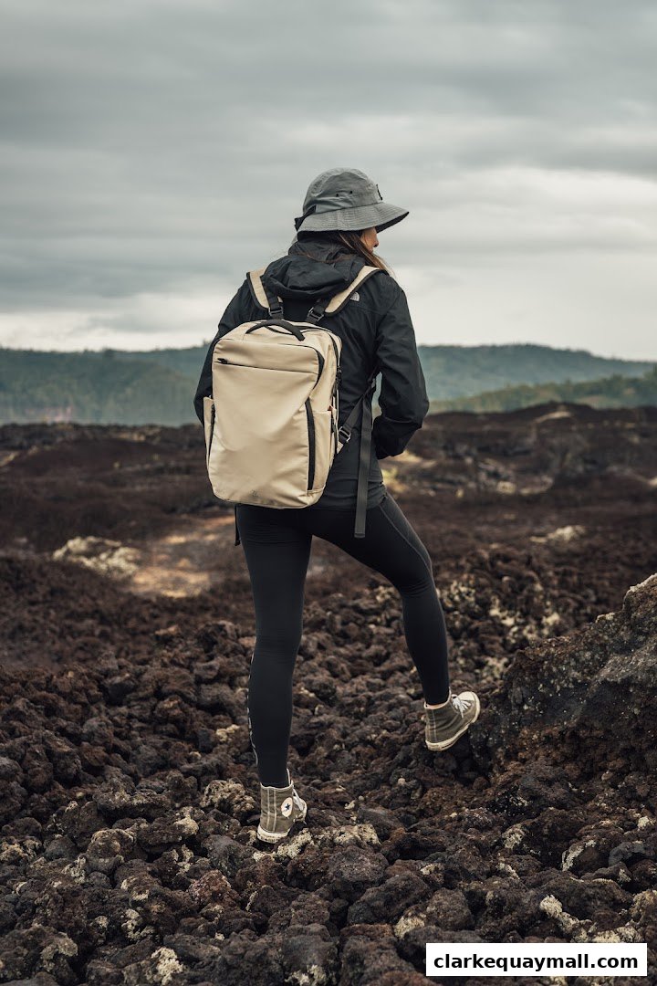 A person wearing a hat, jacket, and backpack walks on a rocky, volcanic terrain.