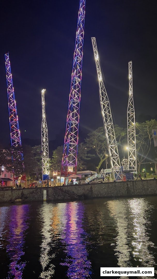 Tall amusement rides illuminated with colorful lights at night, reflected in the water.