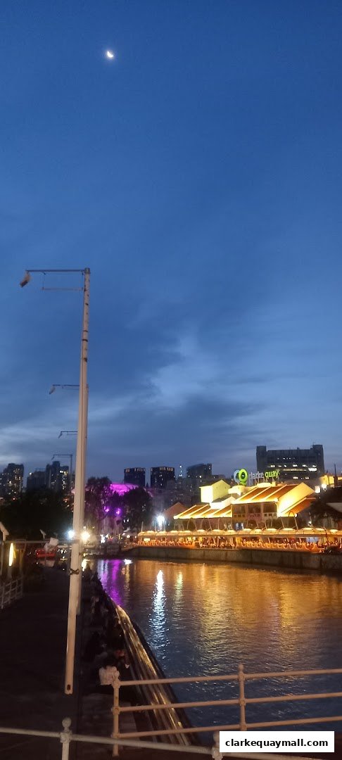 A scenic view of Clarke Quay at dusk with illuminated buildings and a river.