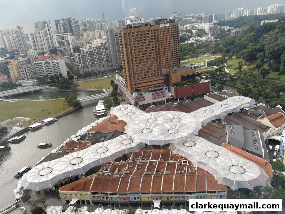 Aerial view of a riverside shopping complex with distinctive white canopies and surrounding cityscape.