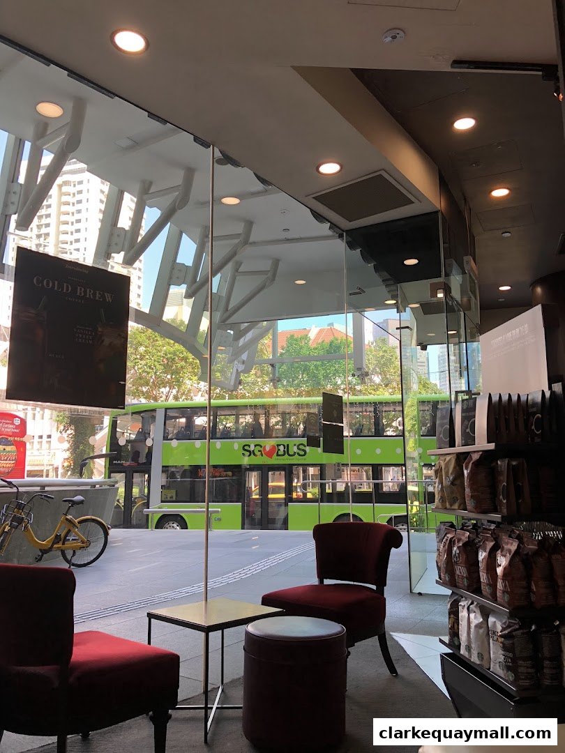 Interior view of a coffee shop with seating and merchandise, looking out at a street scene.