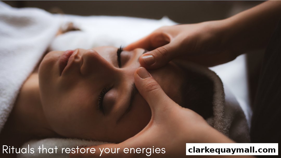 A person receiving a facial massage with closed eyes, wrapped in a white towel.