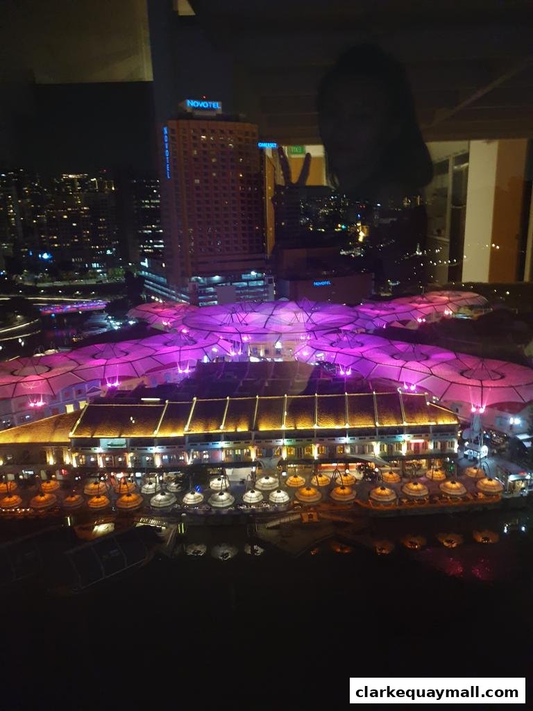 Night view of a waterfront with illuminated buildings and a person's reflection.