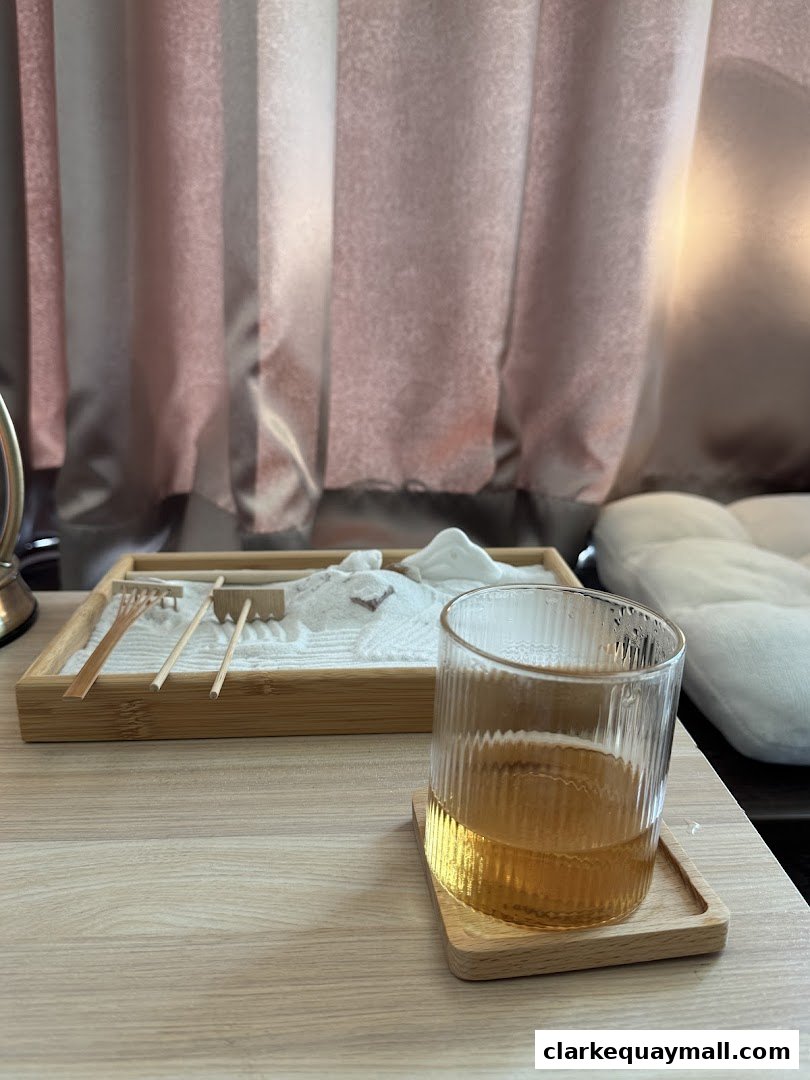 A glass of amber liquid sits on a wooden coaster next to a zen garden.