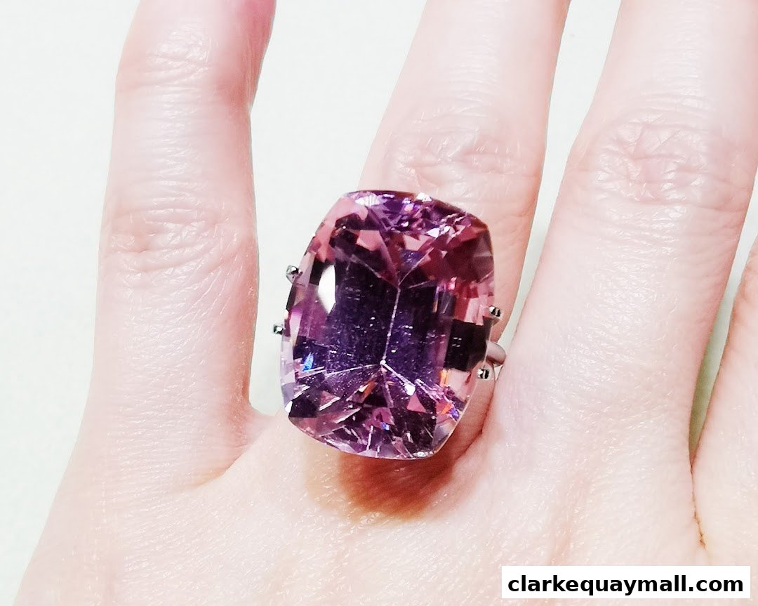 A close-up shot of a large, faceted pink gemstone ring on a person's finger.