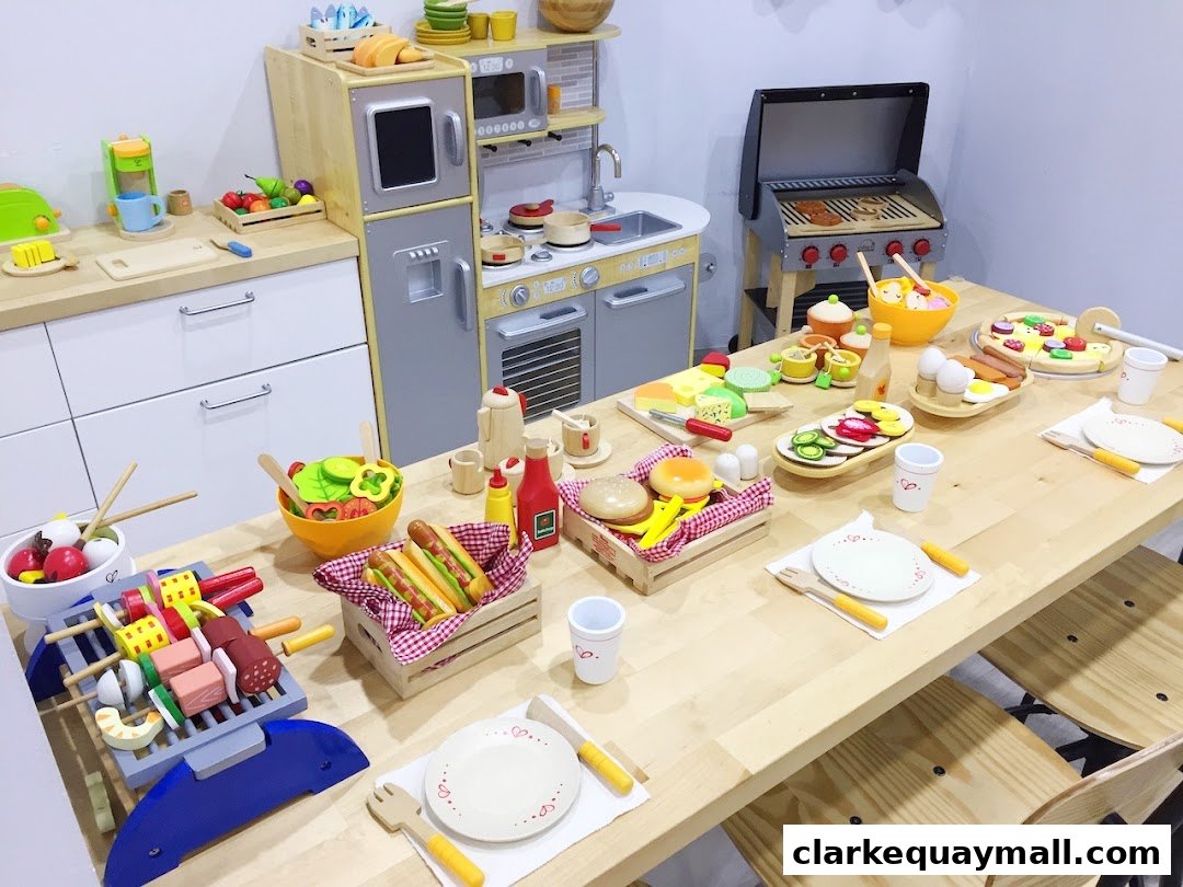 A wooden table set with various toy food items, including a grill, pizza, hot dogs, and salad.