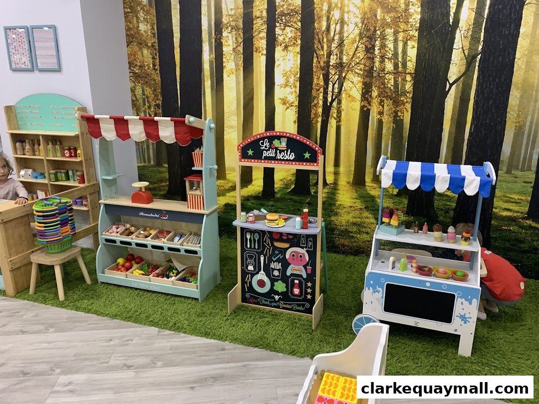 Children's play area with toy food stalls and a forest-themed backdrop.