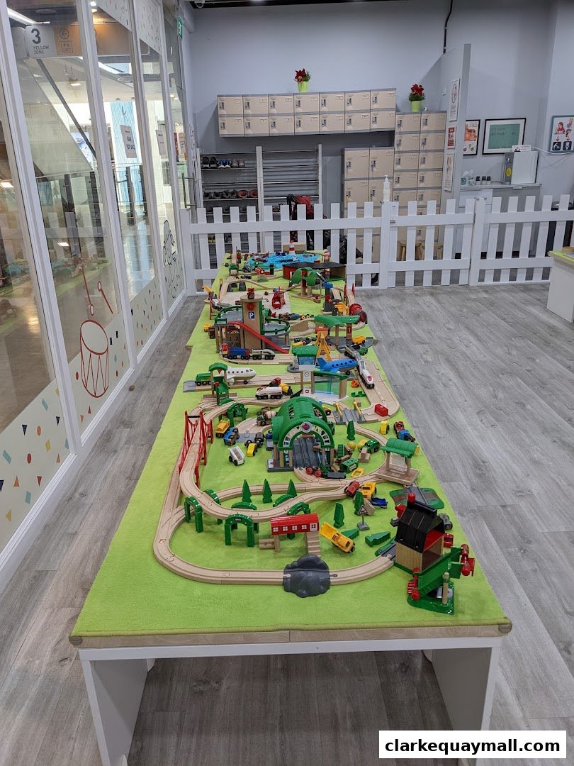 A long table covered in a green mat displays an elaborate wooden train set with tracks, trains, and accessories.