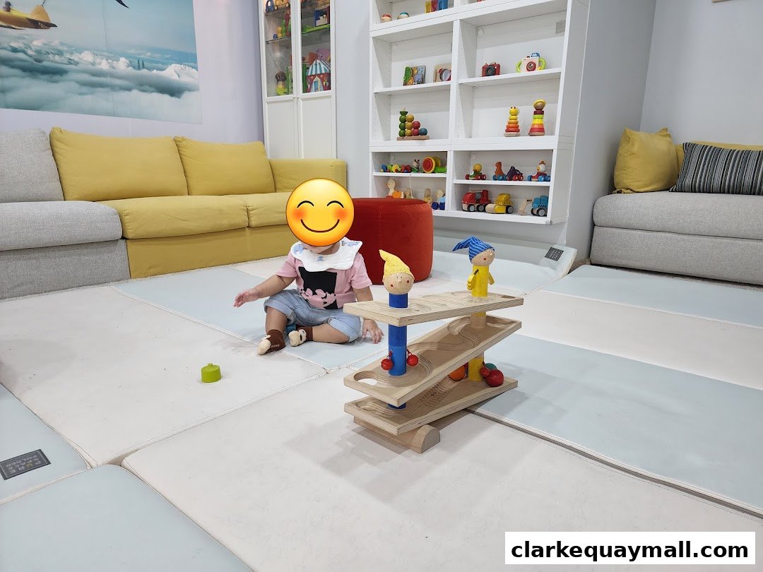 A child plays with a wooden toy car ramp in a brightly lit room with shelves of toys.