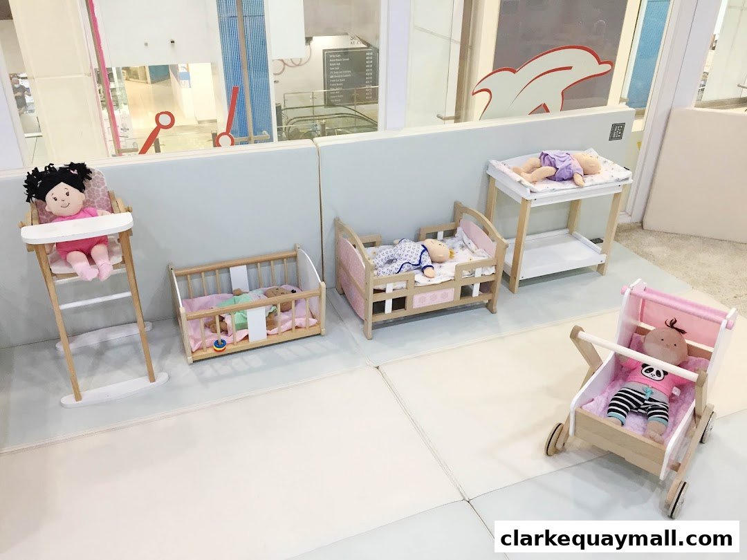 Dolls are displayed in a play area with toy furniture like a high chair, crib, and stroller.