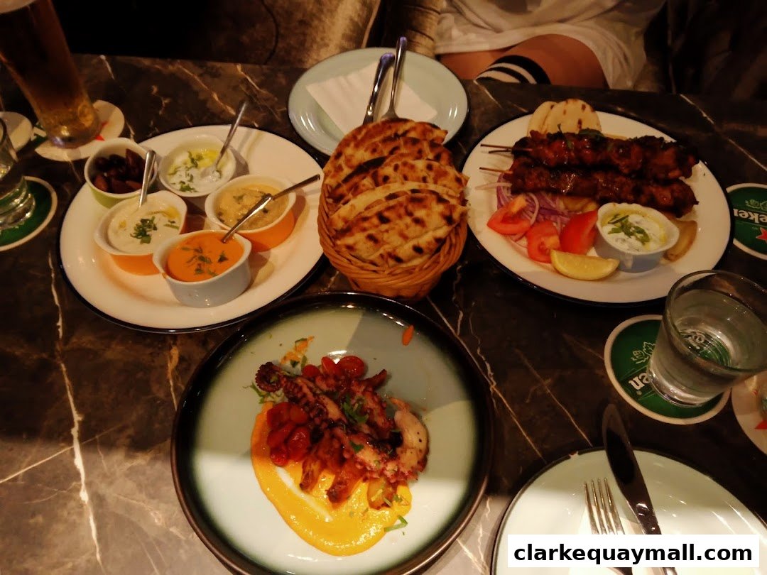 A table laden with delicious Mediterranean dishes, including dips, skewers, and grilled octopus.
