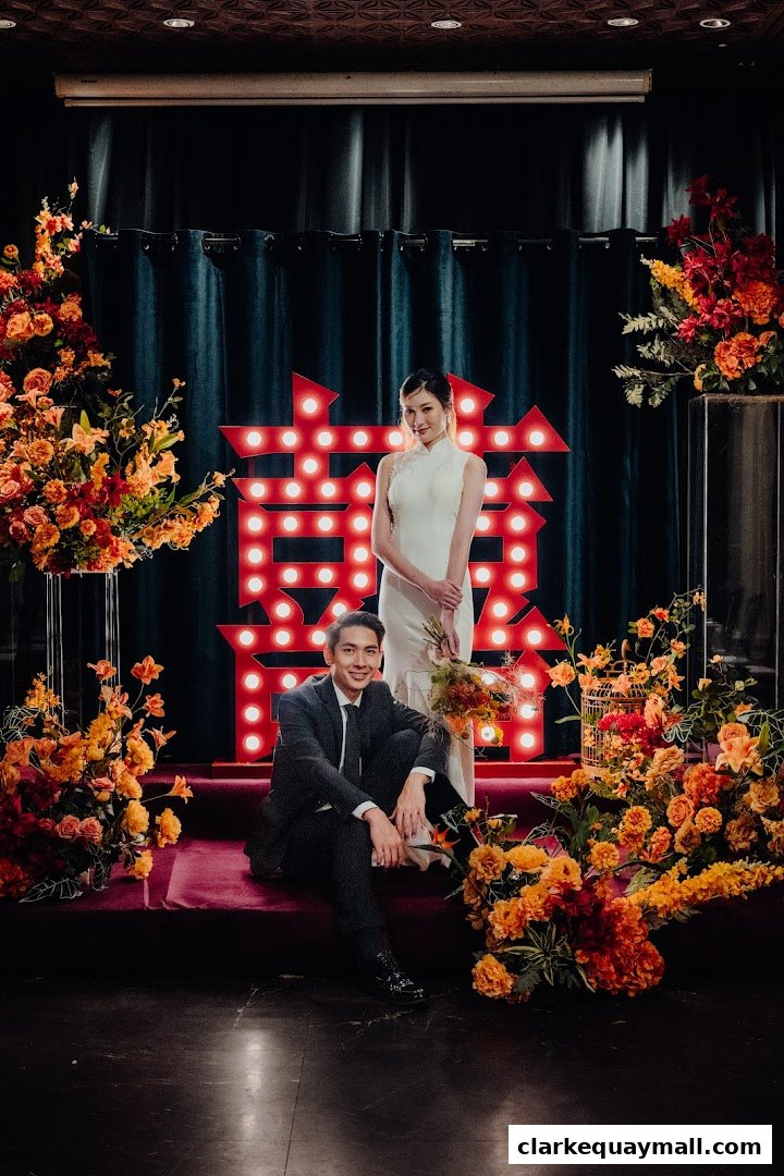 A couple poses in front of a large illuminated Chinese character with floral arrangements.
