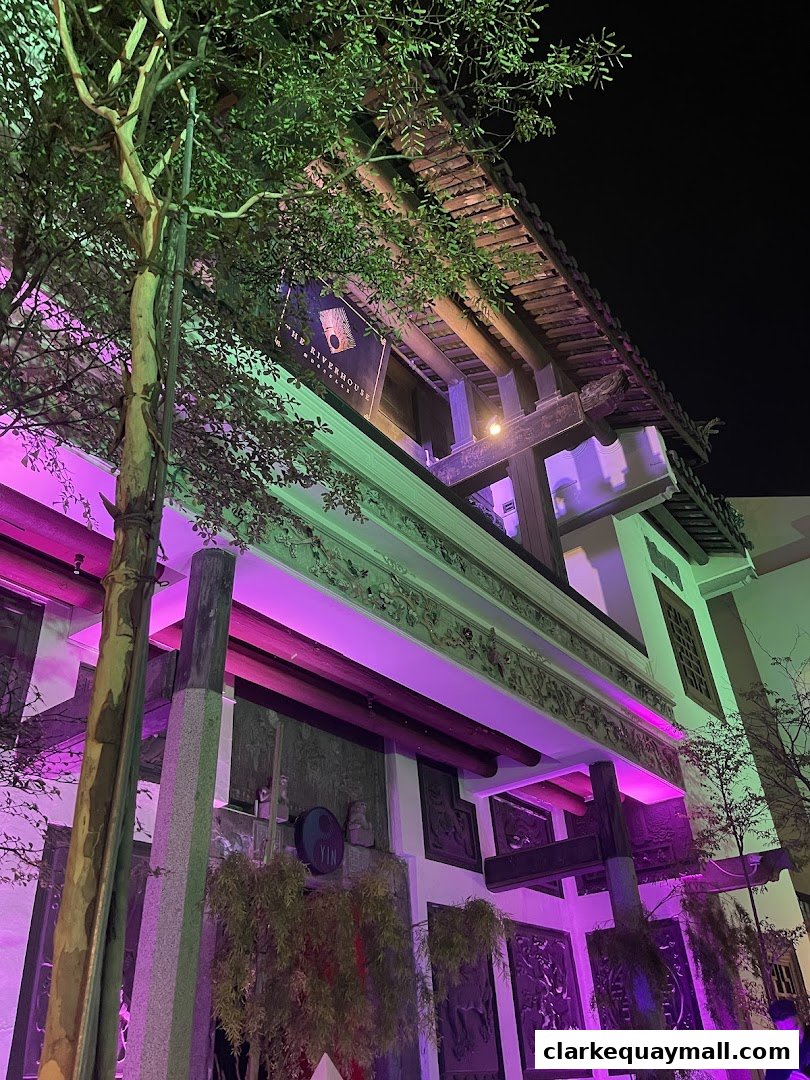The Riverhouse Singapore building facade at night, illuminated with purple and green lights.
