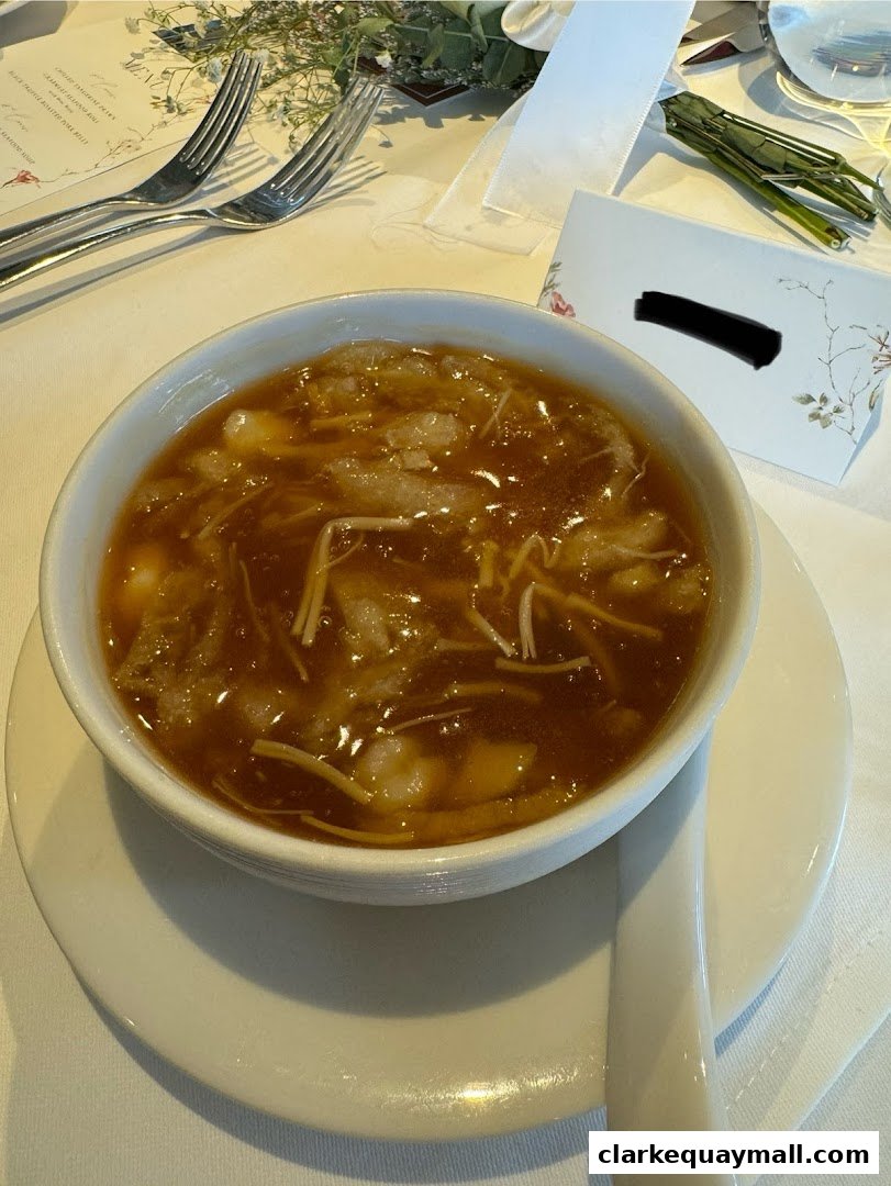 A close-up of a bowl of soup with seafood and noodles, served at a formal setting.