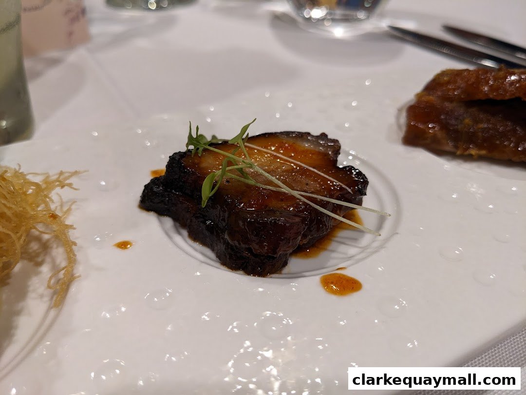 A close-up of a gourmet dish featuring glazed pork belly with a side of crispy noodles.