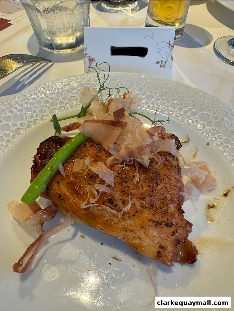 A close-up of a beautifully plated dish with grilled fish, garnished with delicate shavings and a green vegetable.