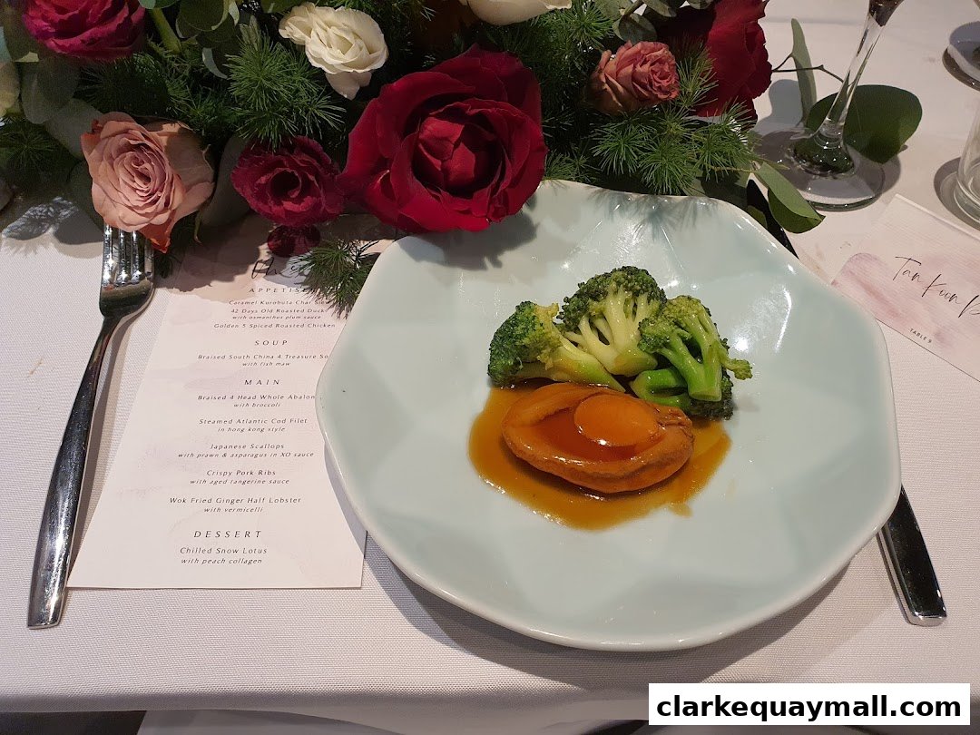A table setting with a menu, a plate of abalone and broccoli, and floral decorations.