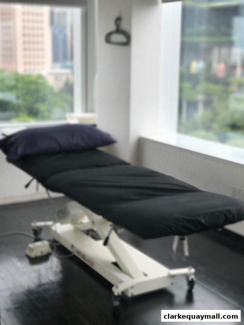 A black massage table with a pillow sits near a window with a city view.