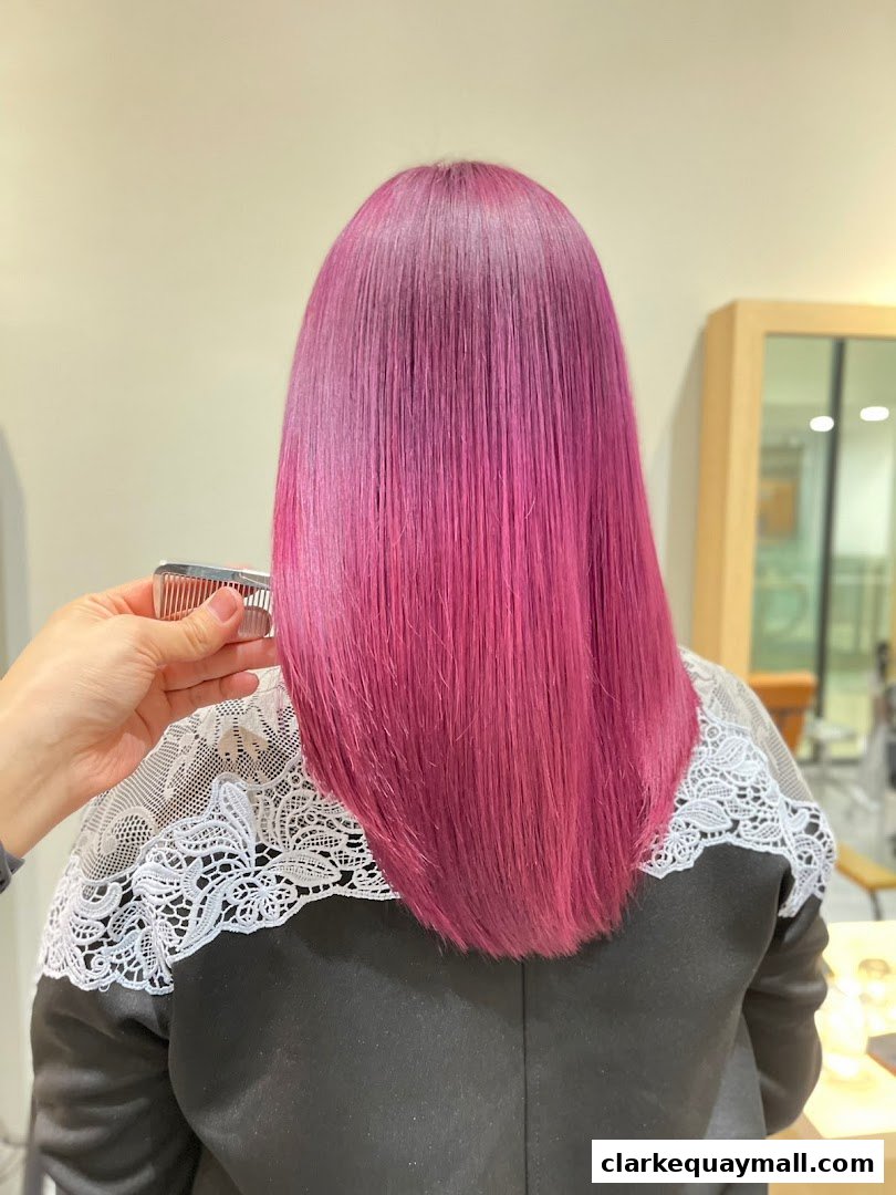A person's back with vibrant pink hair being styled with a comb.