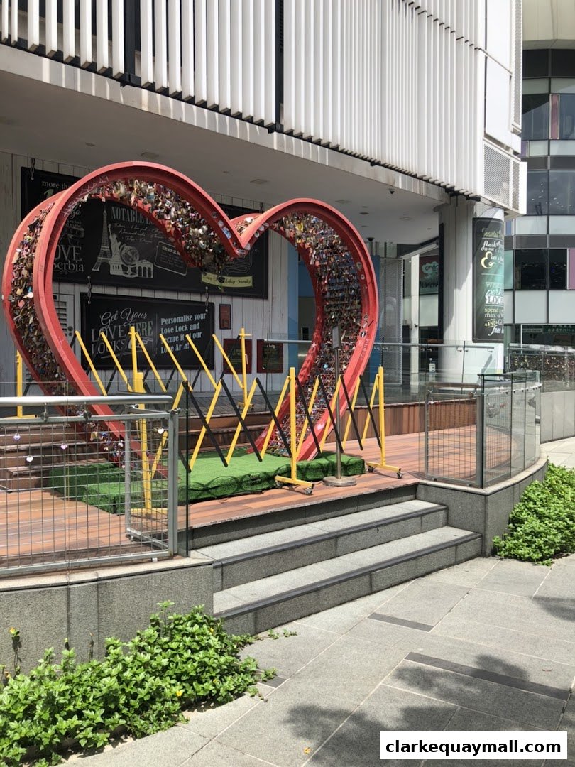 A large red heart sculpture filled with locks, set against a modern building facade.