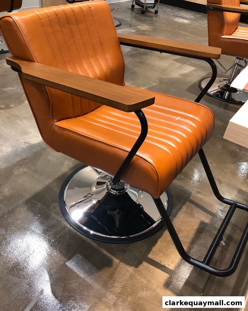 A stylish, orange leather salon chair with wooden armrests and a chrome base.