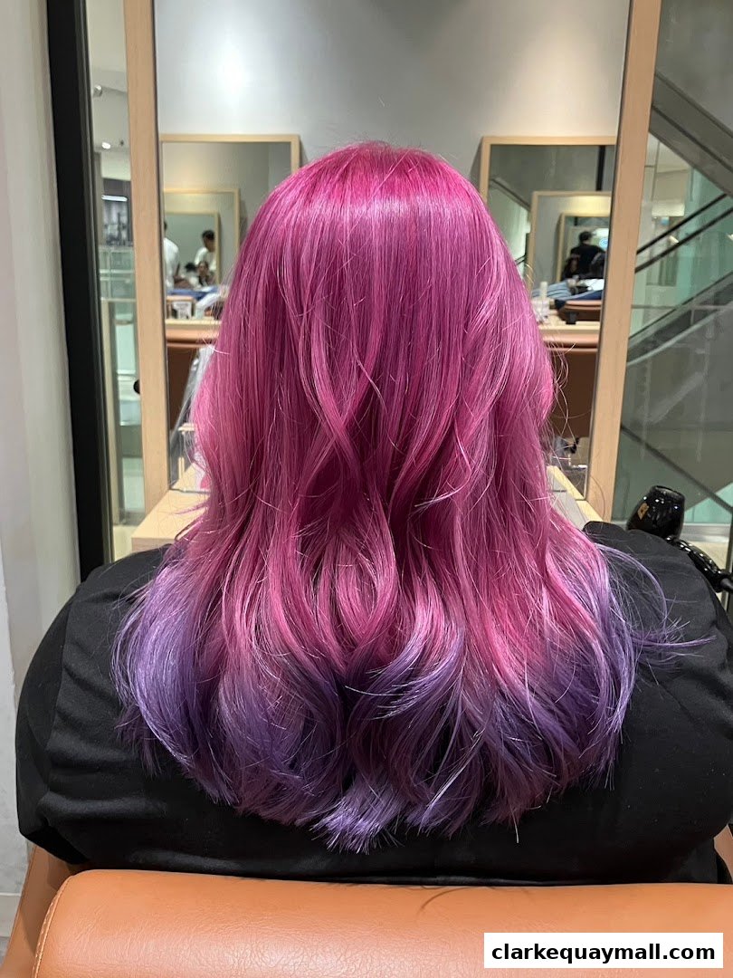 A person with vibrant pink and purple ombre hair sitting in a salon chair.