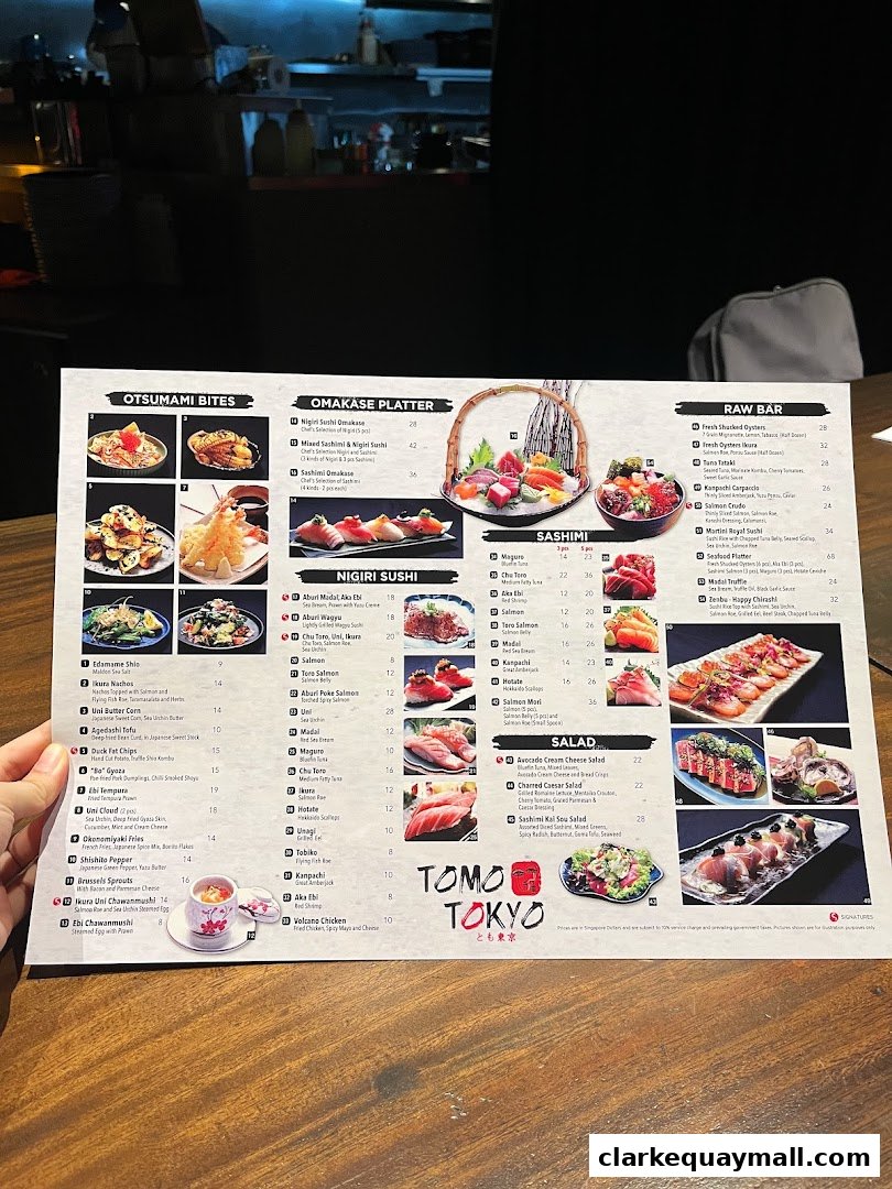 A person holding a menu from Tomo Tokyo, showcasing various sushi and sashimi dishes.