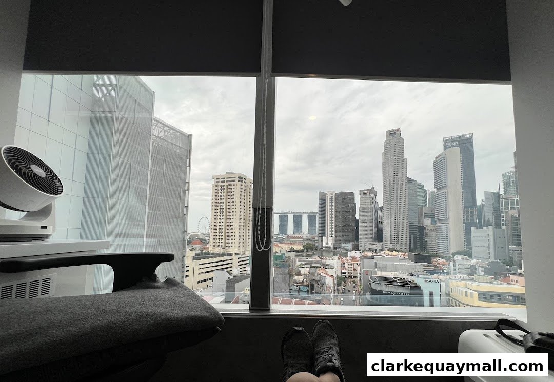 A view from a window overlooking a city skyline with a chair and fan in the foreground.